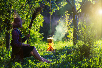 young witch by  fire in magic forest makes in cauldron magic potion