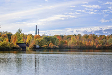 The quiet lake which reflects autumnal leaves and 2 pipes of an old factory in the background