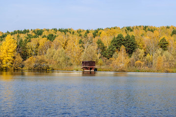 The Boat Shed on quiet colorful lake that reflects autumn leaves, blue sky 