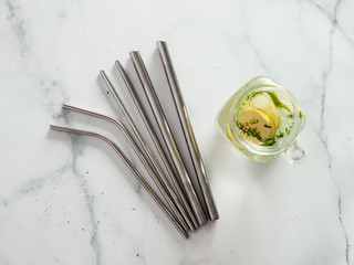Metal drinking straws and cold drink in glass mason jar on white marble background. Top view or...