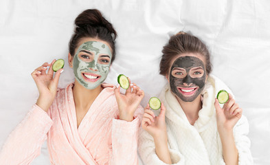 Young friends with facial masks having fun on bed at pamper party, top view