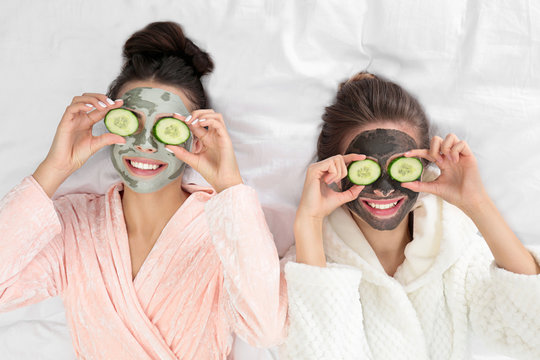 Young friends with facial masks having fun on bed at pamper party, top view