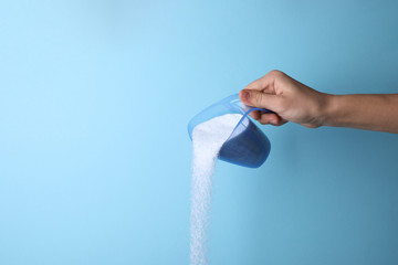 Woman pouring laundry detergent from measuring container against blue background, closeup. Space...
