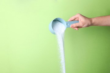 Woman pouring laundry detergent from measuring container against green background, closeup. Space...