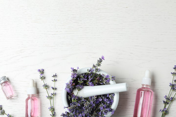 Fototapeta na wymiar Bottles of essential oil, mortar and pestle with lavender flowers on white wooden background, flat lay. Space for text