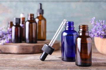 Bottles of lavender essential oil and flowers on wooden table against blue background