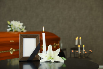 Black photo frame with burning candle and white lily on table in funeral home