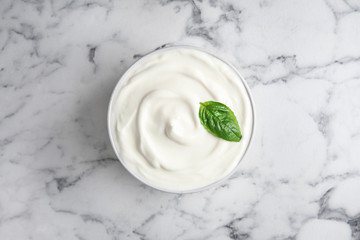Bowl of fresh sour cream with basil on white marble table, top view