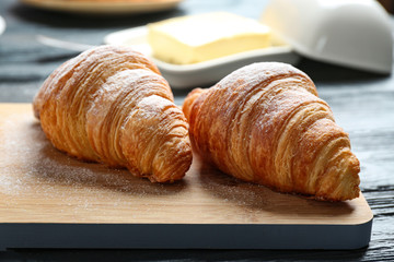 Wooden board with tasty croissants on table, closeup. French pastry