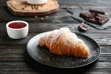 Plate with tasty croissant and powdered sugar on dark wooden table. French pastry