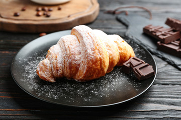 Plate of tasty croissant with powdered sugar and chocolate on dark wooden table. French pastry
