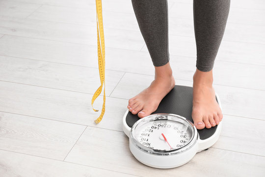 Woman with tape standing on scales indoors, space for text. Overweight problem