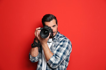 Young professional photographer taking picture on red background - obrazy, fototapety, plakaty