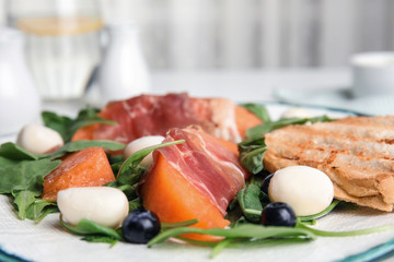 Fresh melon with prosciutto, mozzarella and arugula on plate, closeup