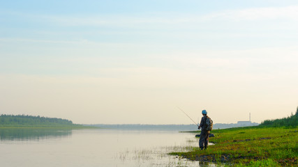 Yakut Asian girl tourist fisherman with a backpack and a cap to fish in the river vilyu in the haze at sunset in the wild North of Russia on the background of the village Suntar.