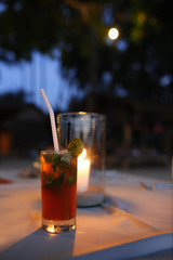 A mojito cocktail glass on a background of a burning candle on a table in a restaurant with evening lighting.