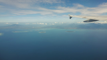 Blue sea or ocean in it and small tropical islands. Looking through window aircraft during flight