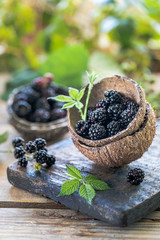 Two coconut halves stuffed by ripe blackberry on an old wooden board.