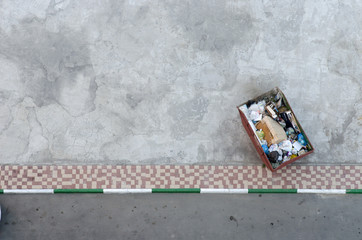 Trash the urn is on the asphalt road next to the sidewalk is filled with garbage bags and boxes. The view from the top.