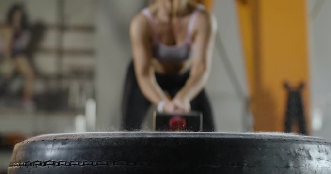 Young woman hits a tire with a sledgehammer, crossfit training with hammer.