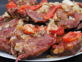 Appetizing and beautiful smoked pork ribs are stewed in a sauce with tomatoes , onions and herbs on a white plate. High-calorie and tasty isolated meat dish close-up