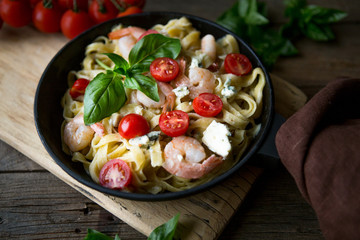 Tagliatelle pasta with shrimps and tomato sauce on dark background. Italian cuisine. Top view