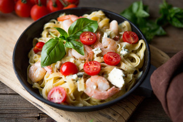 Tagliatelle pasta with shrimps and tomato sauce on dark background. Italian cuisine. Top view