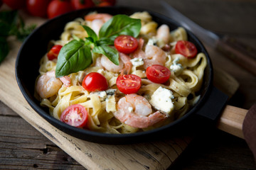 Tagliatelle pasta with shrimps and tomato sauce on dark background. Italian cuisine. Top view