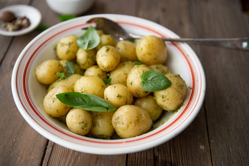 Potato. Tasty Young boiled potatoes with basil in white bowl on rustic wooden table.