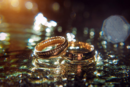 Gold wedding rings of bride and groom in shiny water spray, bright background, selective focus. Wedding accessories and jewelry.