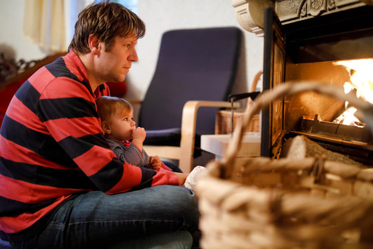 Middle age father sitting by fireplace with cute little baby girl at home. Happy family, dad with daughter make fire for Christmas time. Safe handling for kids - Powered by Adobe