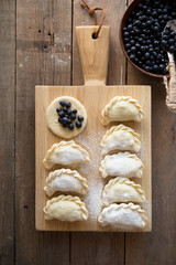 Preparing dumplings filled with blueberry. Elderly female hands making pierogi or pyrohy, varenyky, vareniki. Traditional Ukrainian cuisine, bakery product, sprinkled flour.
