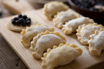 Preparing dumplings filled with blueberry. Elderly female hands making pierogi or pyrohy, varenyky, vareniki. Traditional Ukrainian cuisine, bakery product, sprinkled flour.