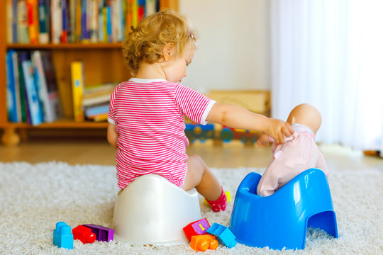Closeup of cute little 12 months old toddler baby girl child sitting on potty. Kid playing with doll toy. Toilet training concept. Baby learning, development steps