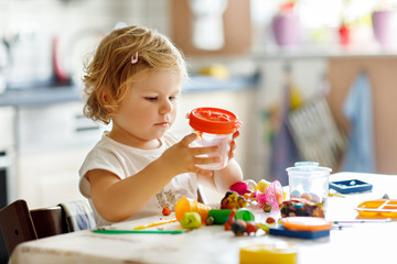 Adorable cute little toddler girl with colorful clay. Healthy baby playing and creating toys from...