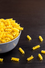 black background with italian raw pasta spiral fusilli in bowl with copy space