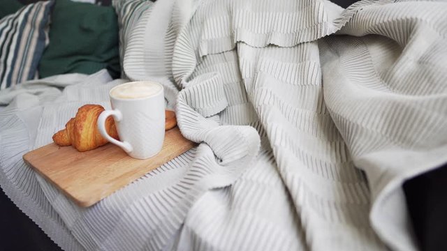 Static shot - fresh coffee and a hot croissant on a large sofa with pillows, blankets and a plaid. Hygge or Lagom concept