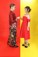 Two Asian woman traditional kebaya and modern dress red yellow paper background meet great