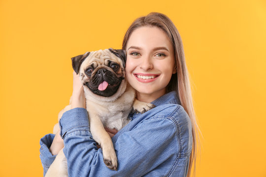 Beautiful young woman with cute pug dog on color background