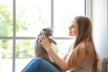 Beautiful woman with cute cat sitting near window