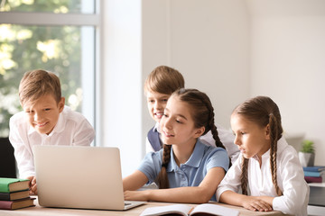 Cute little pupils with laptop in classroom