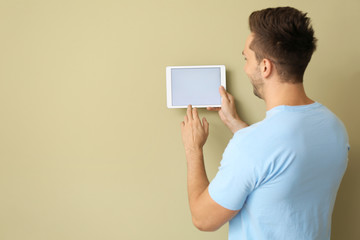 Young man with modern tablet computer near wall