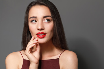 Beautiful young woman with bright lipstick on grey background