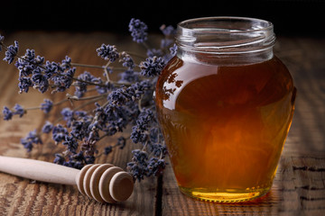 Honey in a glass jar, a spoon for honey, lavender flowers on an old wooden table.