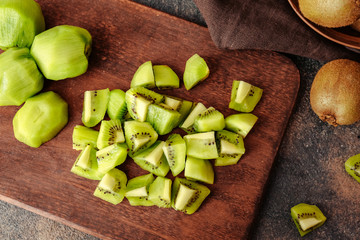 Board with tasty cut kiwi on grunge background