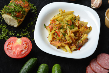 Fried potatoes in a white plate on a black background, spicy food
