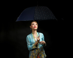 Asian woman in tractional kebaya carrying umbrella on black background