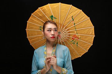 Asian woman in tractional kebaya behind umbrella on black background
