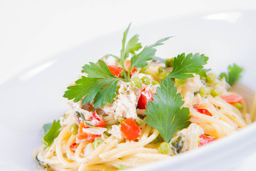 Spaghetti with cream sauce with smoked mackerel, peas ,bell pepper and some parsley on a white plate on a white background