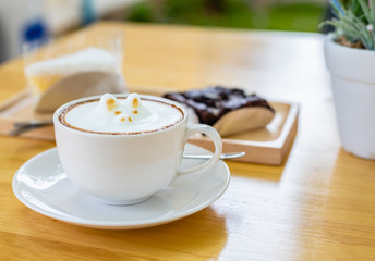 White cup of coffee latte with cute cat shape latte art milk foam on wood table.